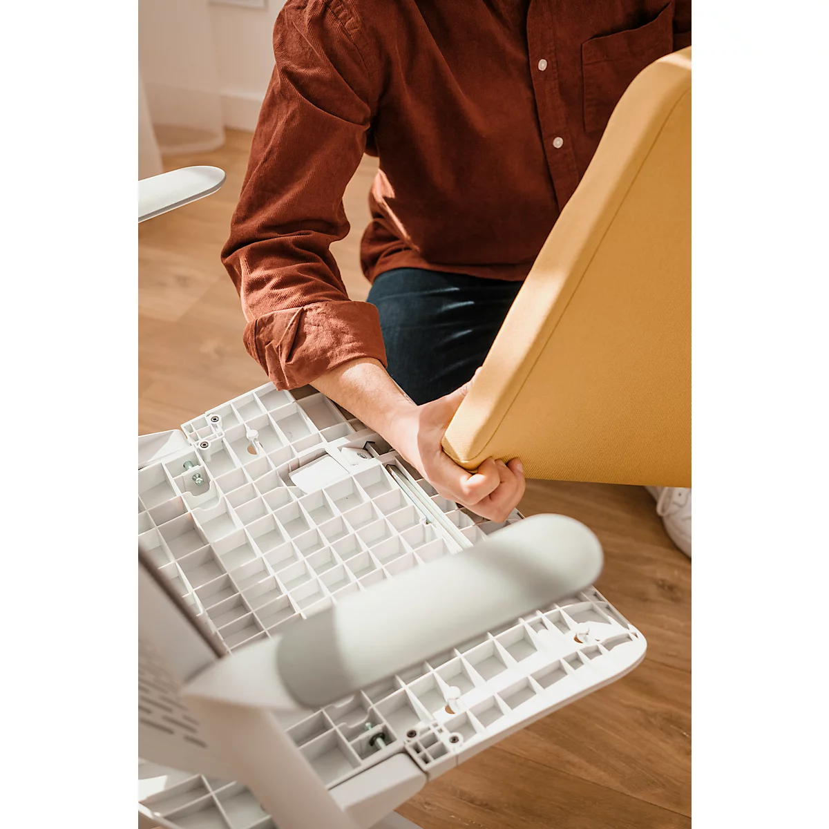 Person assembling chair: Holds yellow seat, which is attached to a white frame. Detailed shot.