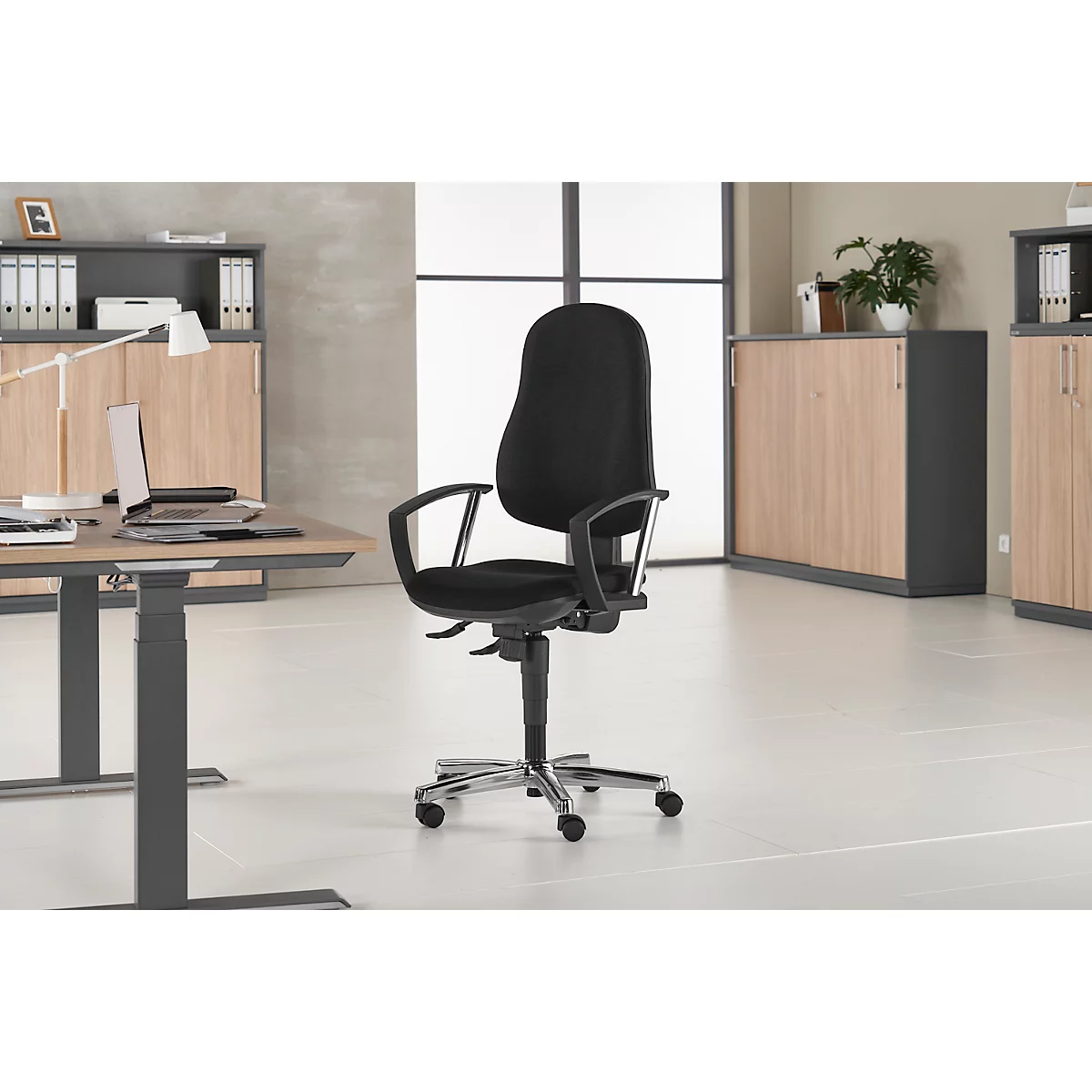 Black office chair in a modern office. The chair has armrests and a chrome-plated base.