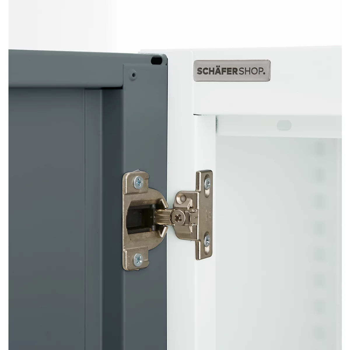 Close-up of a cabinet hinge. Gray door on the left, white door on the right. In between, the metal hinge with screws.