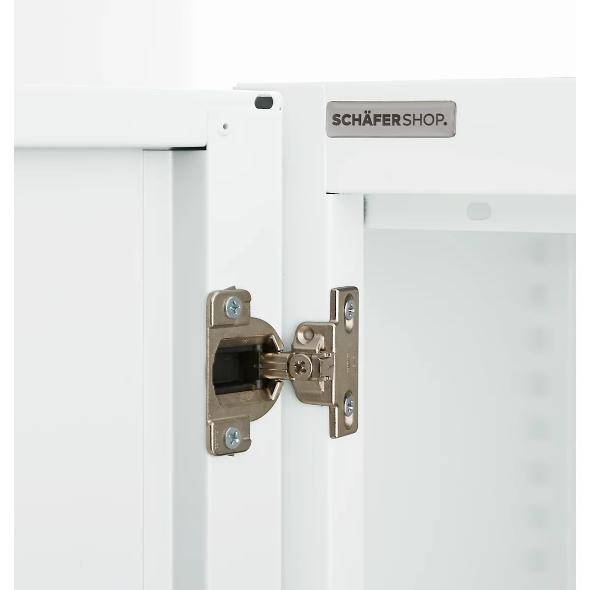 Close-up of a cabinet hinge. The cabinet is white with a silver hinge. The lettering Schäfershop is visible.