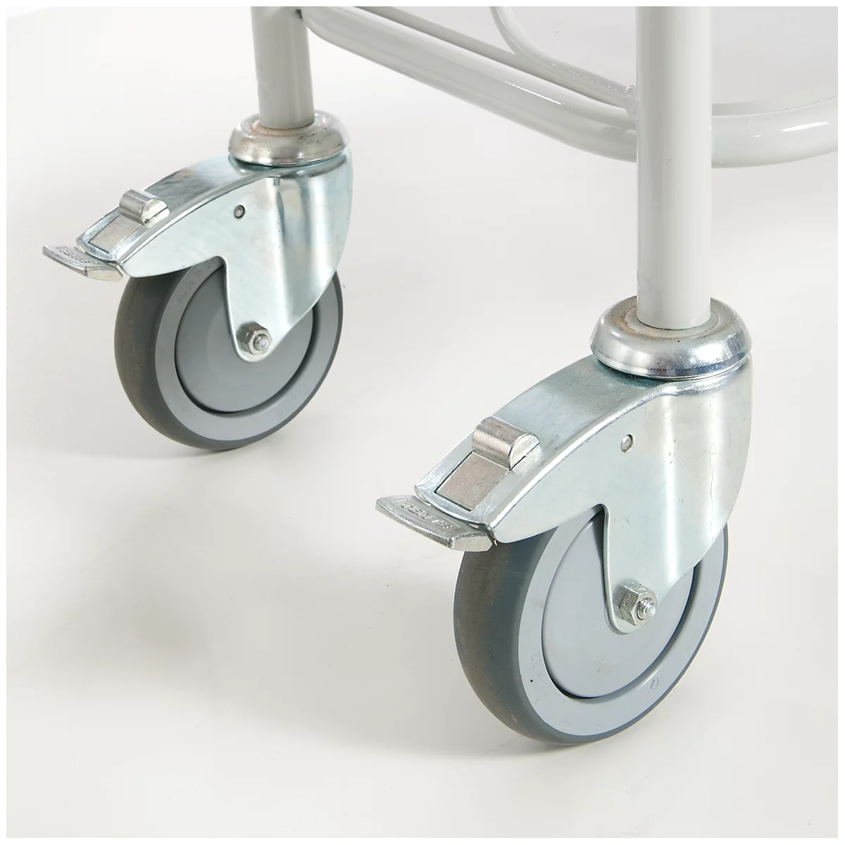 Close-up of two casters with brakes, mounted on a metal frame. The casters are gray, the frame parts are silver.