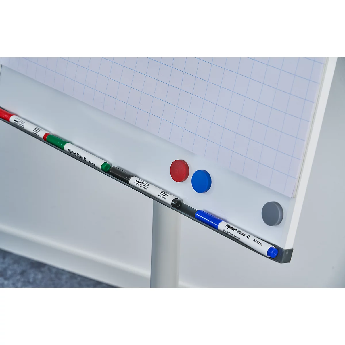 Gros plan sur un tableau blanc avec des marqueurs rouges, verts, noirs et bleus, à côté d'aimants rouges, bleus et gris.