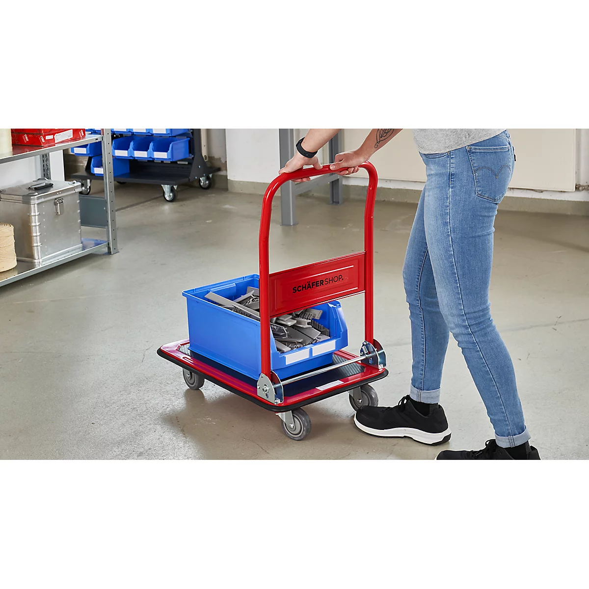 Une personne tire un chariot rouge avec une boîte bleue. Inscription : SCHAEFER SHOP.