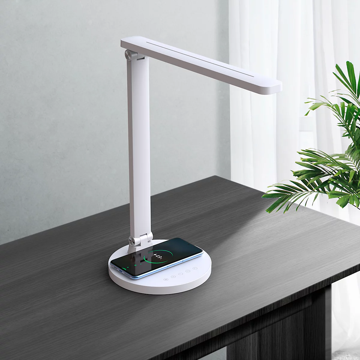 Witte bureaulamp met geïntegreerd oplaadstation met een smartphone erop. De lamp staat op een donker bureau.