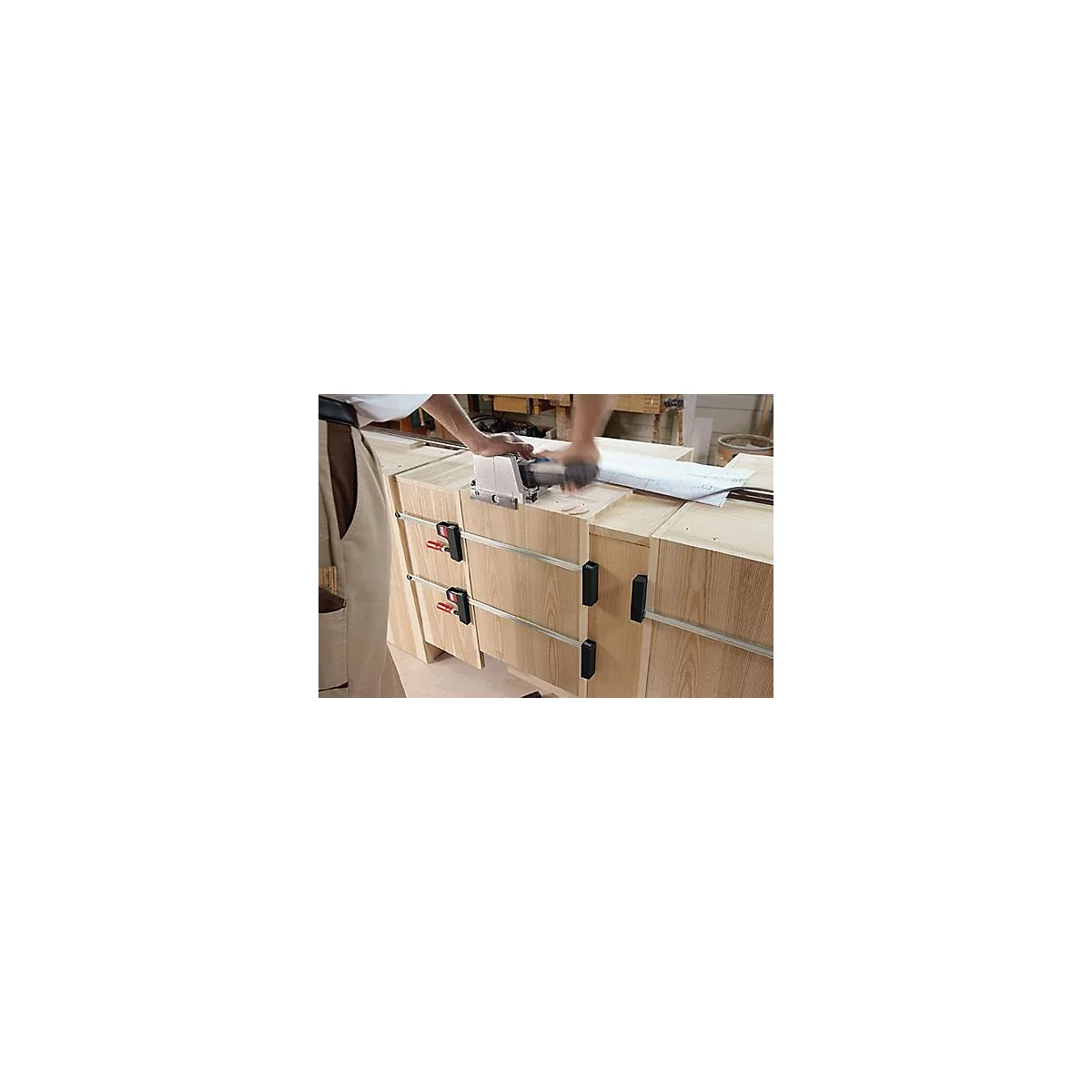 Een timmerman bewerkt hout met een freesmachine op een houten meubelstuk. Klemmen houden de onderdelen bij elkaar.