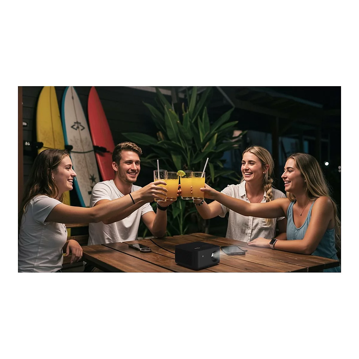 Quatre amis trinquent avec des cocktails. Un petit projecteur est posé sur la table.