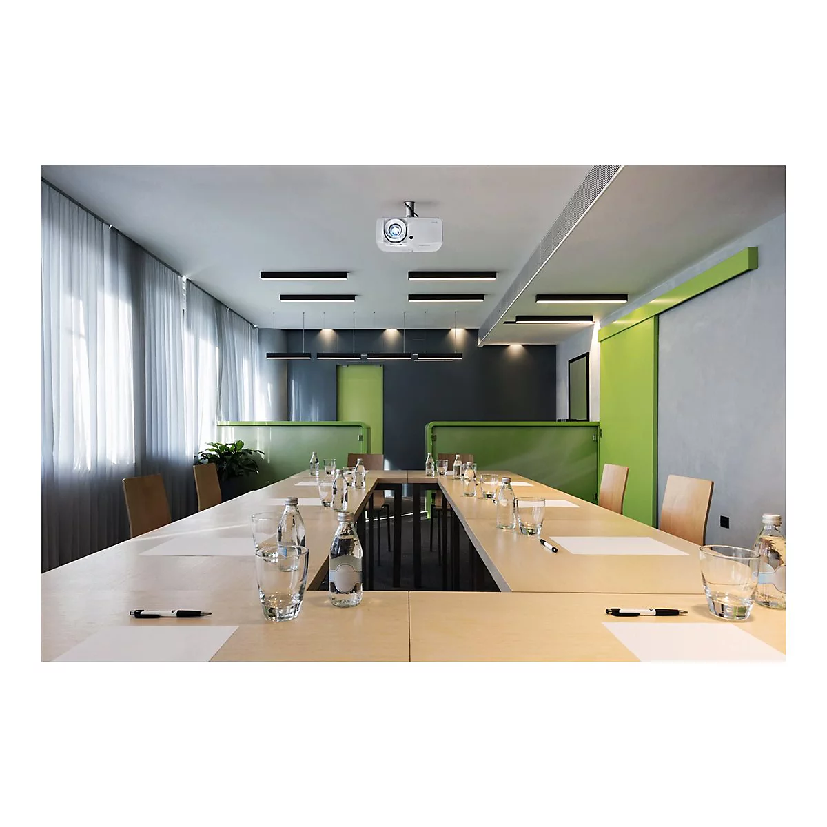 Konferenzraum mit groÃŸem Tisch, StÃ¼hlen, GlÃ¤sern, Flaschen, Stiften und einem Deckenprojektor.