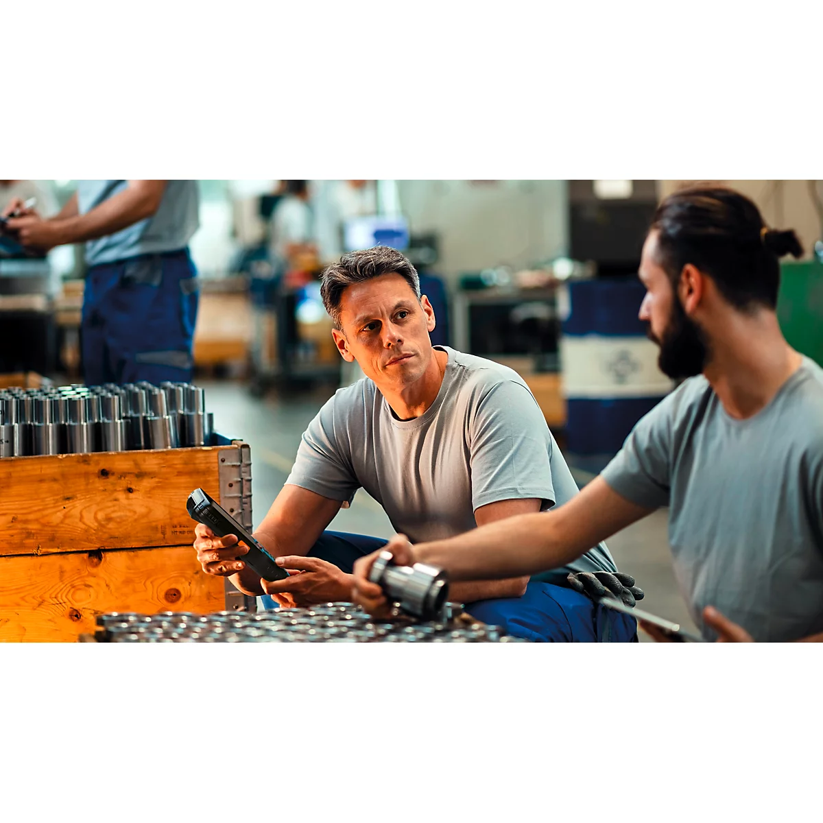 Deux ouvriers d'usine inspectent des composants métalliques à l'aide d'un scanner mobile.