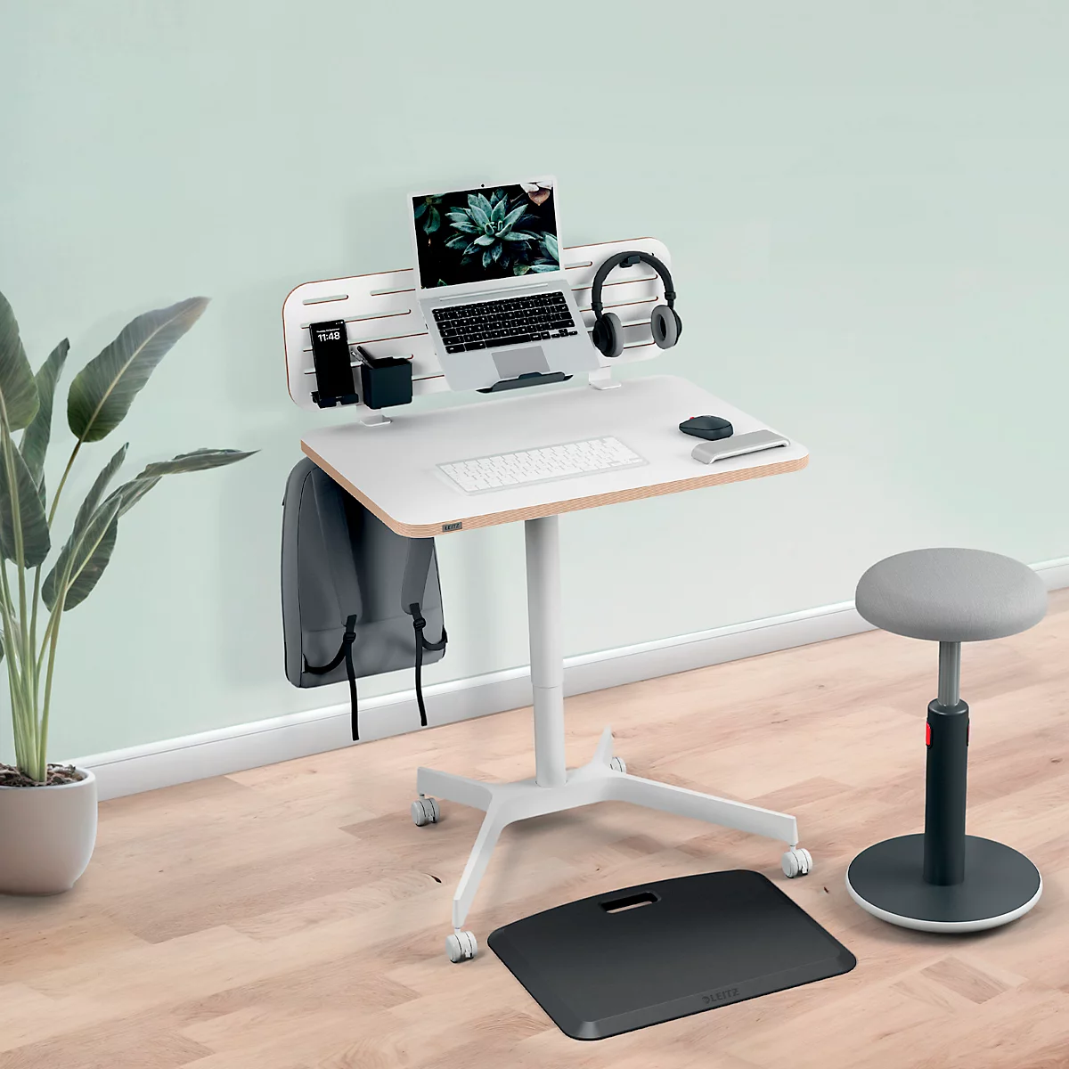 Bureau debout avec ordinateur portable, casque, souris et clavier. Une chaise et un tapis sont placés à côté du bureau.