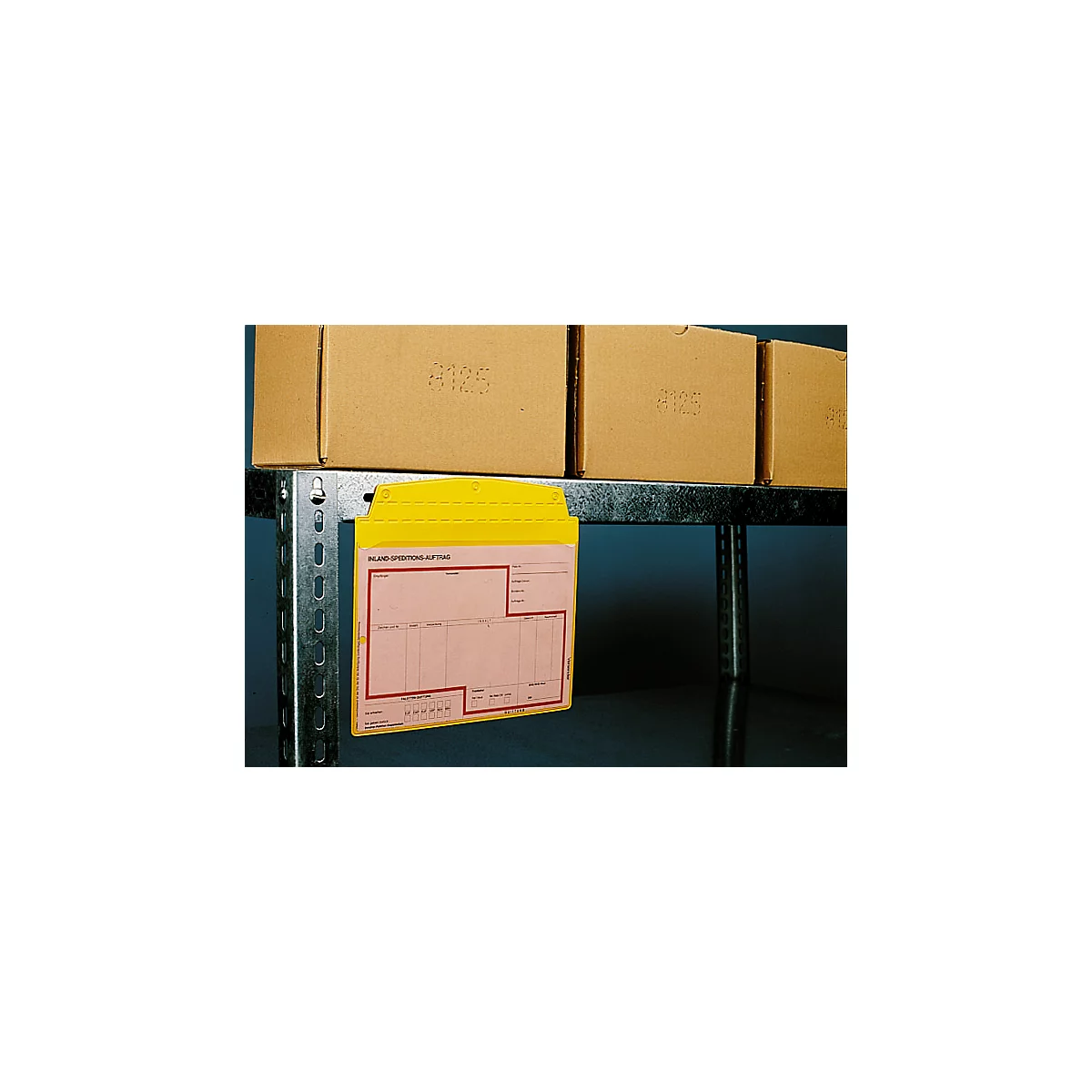 Yellow document holder with paper on a metal shelf, behind cardboard boxes. Text on the paper: Inland Expeditions A/S.