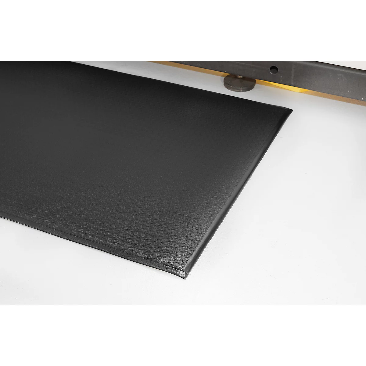 Black, rectangular mat with rounded corners. Shown with part of a structure in the background.
