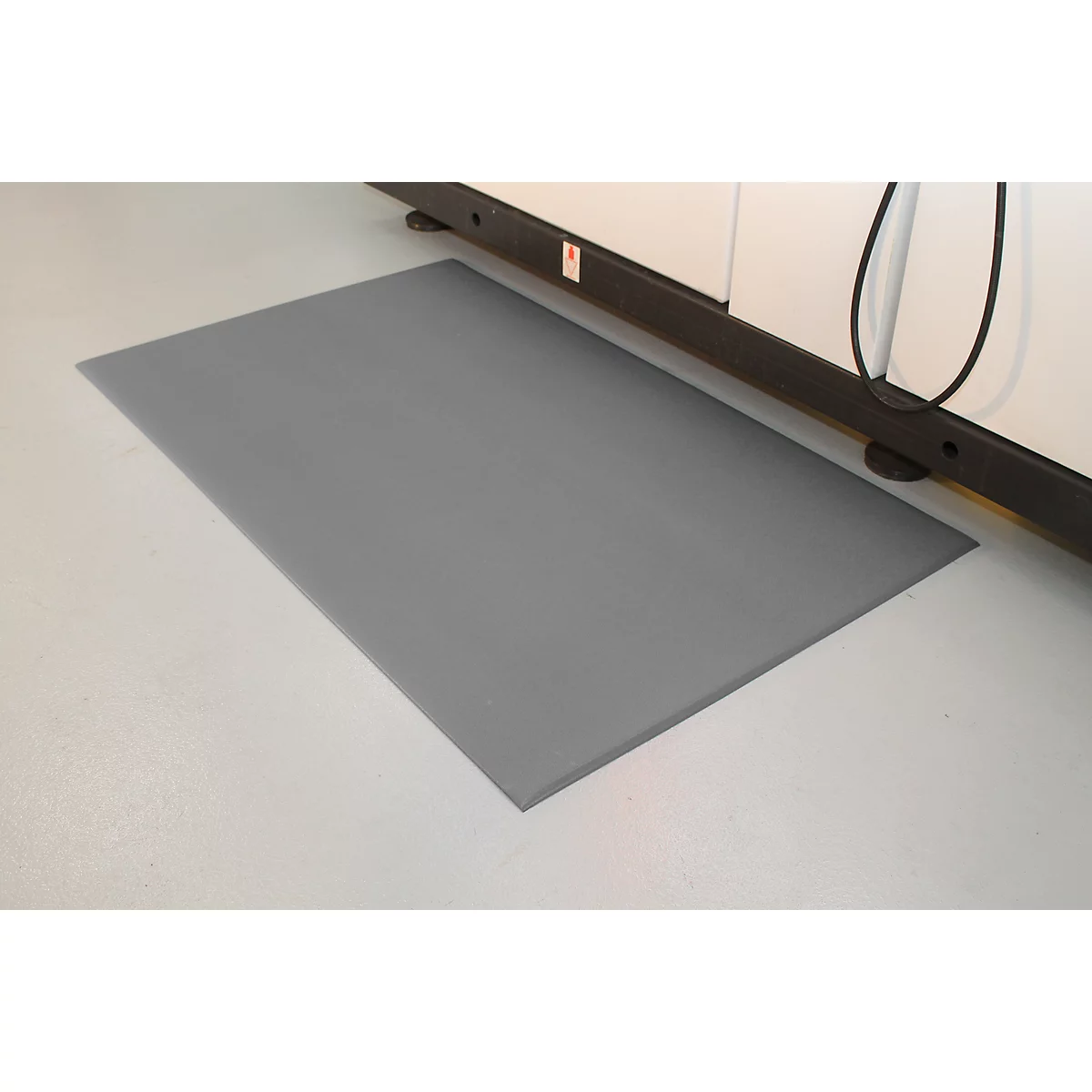 Gray mat in front of a machine on white floor. Black cable and machine parts visible.