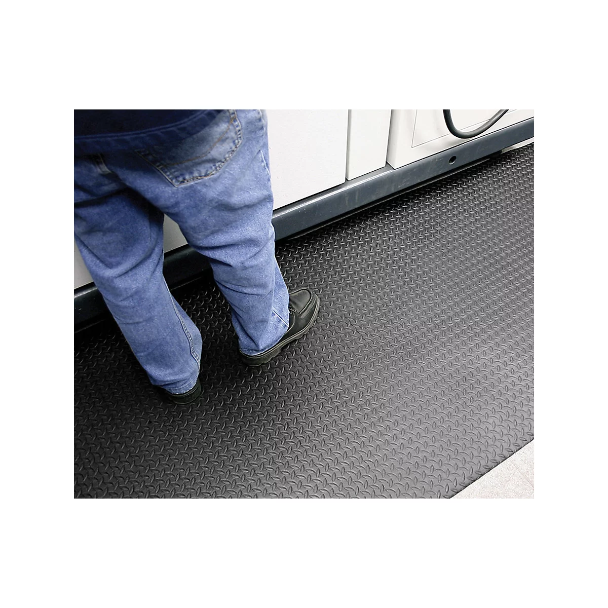 Person standing on a black rubber mat with a diamond pattern in front of a white cabinet.