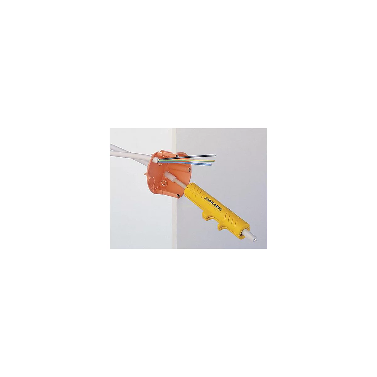 Un boîtier de jonction orange avec des fils et un outil JOKARI jaune. Les outils sont montés sur un mur.