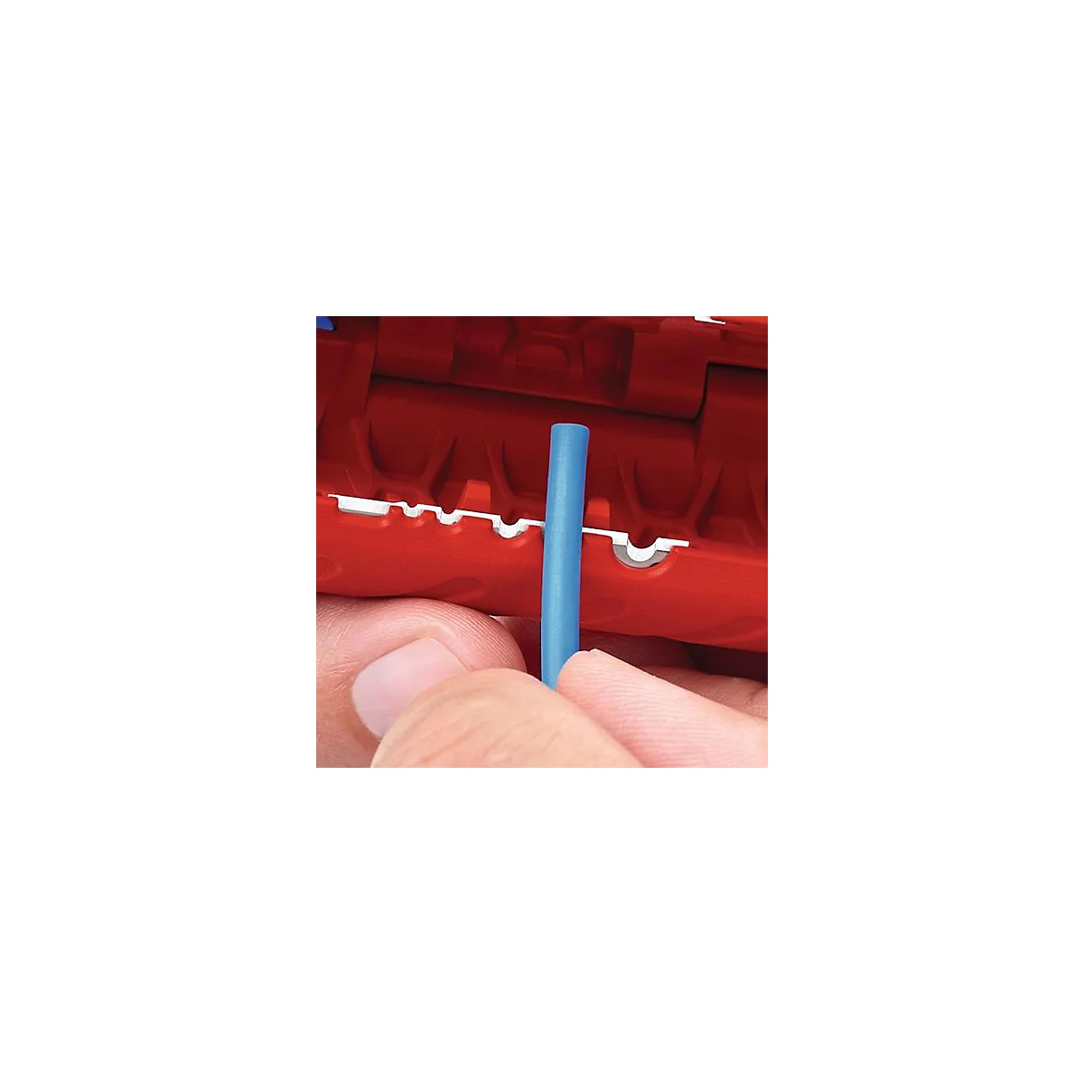 Gros plan d'une pince à dénuder rouge avec un câble bleu. La pince est tenue par une main.