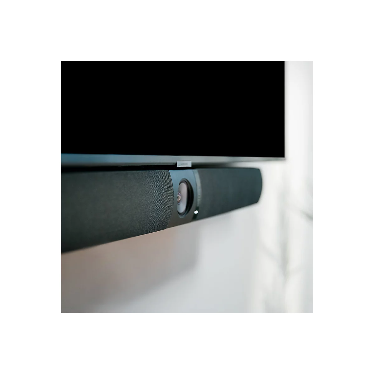 Ein schwarzer Soundbar unter einem schwarzen Fernseher, vor einer weißen Wand. Der Soundbar ist detailreich.