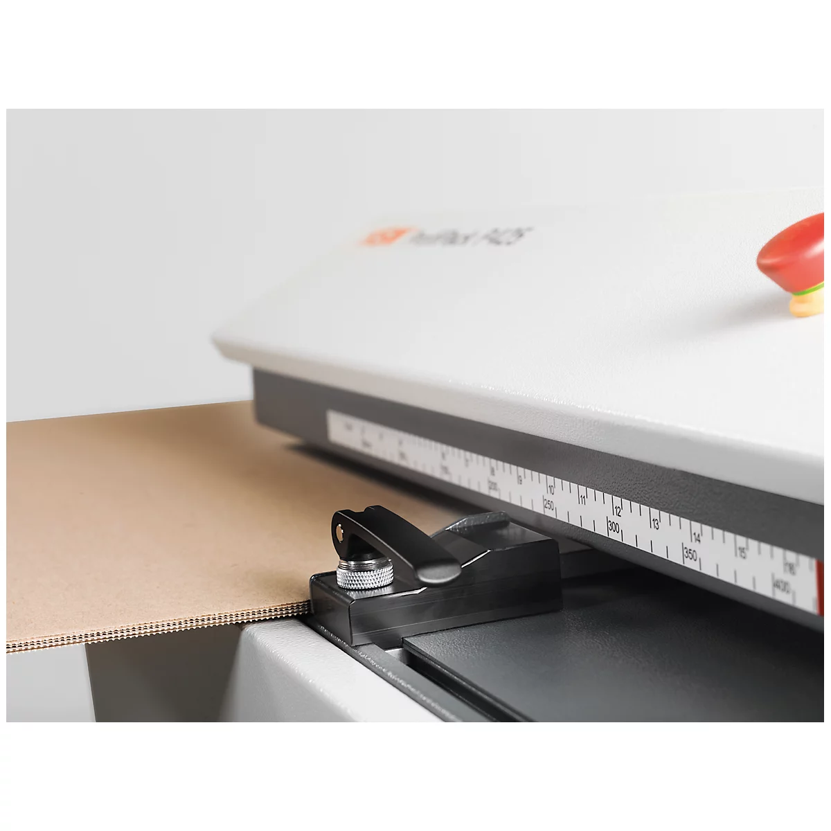 Close-up of cardboard in a paper cutter. A red button and a scale are visible on the machine.