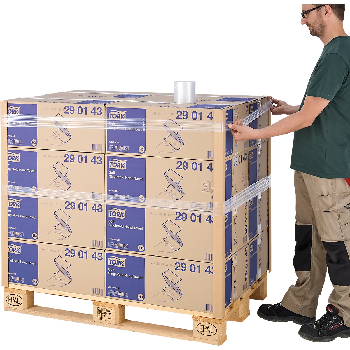 Ein Mann verpackt eine Palette mit Papierhandtuch-Kartons mit Folie. Die Paletten sind mit 'Tork' und '29 01 4' beschriftet.