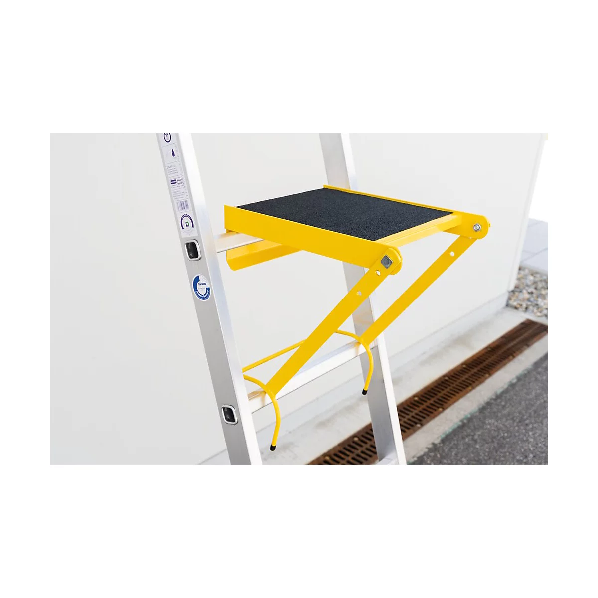 Échelle escabeau jaune avec une surface noire antidérapante. L'échelle est placée devant un mur blanc.