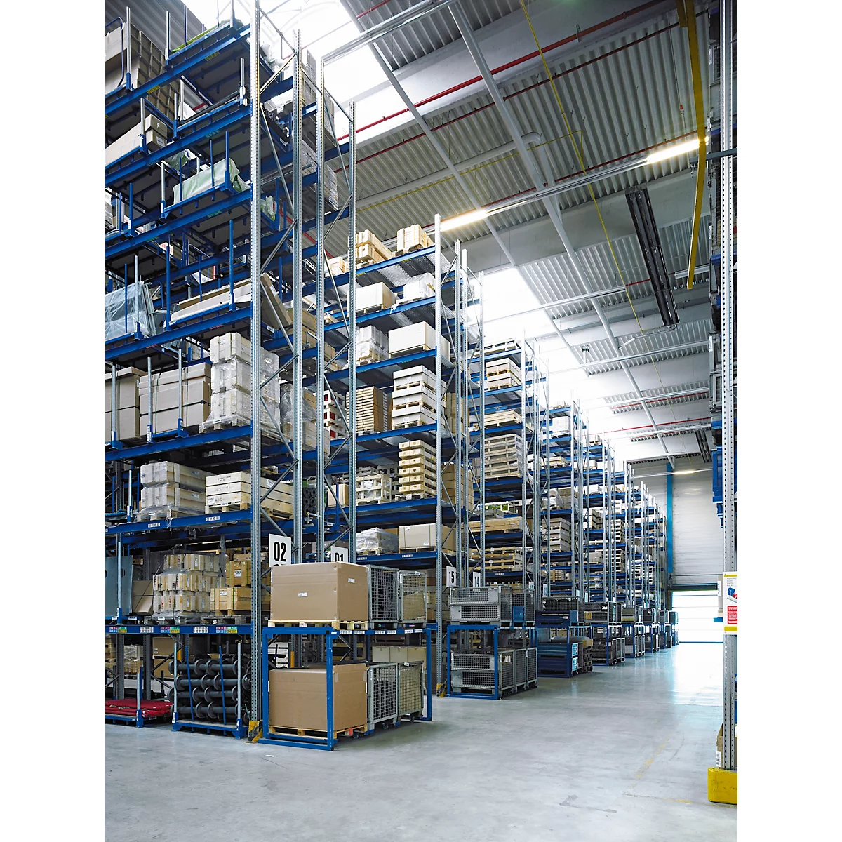 Groot magazijn met planken vol dozen en pallets. Helder plafond met dakramen.