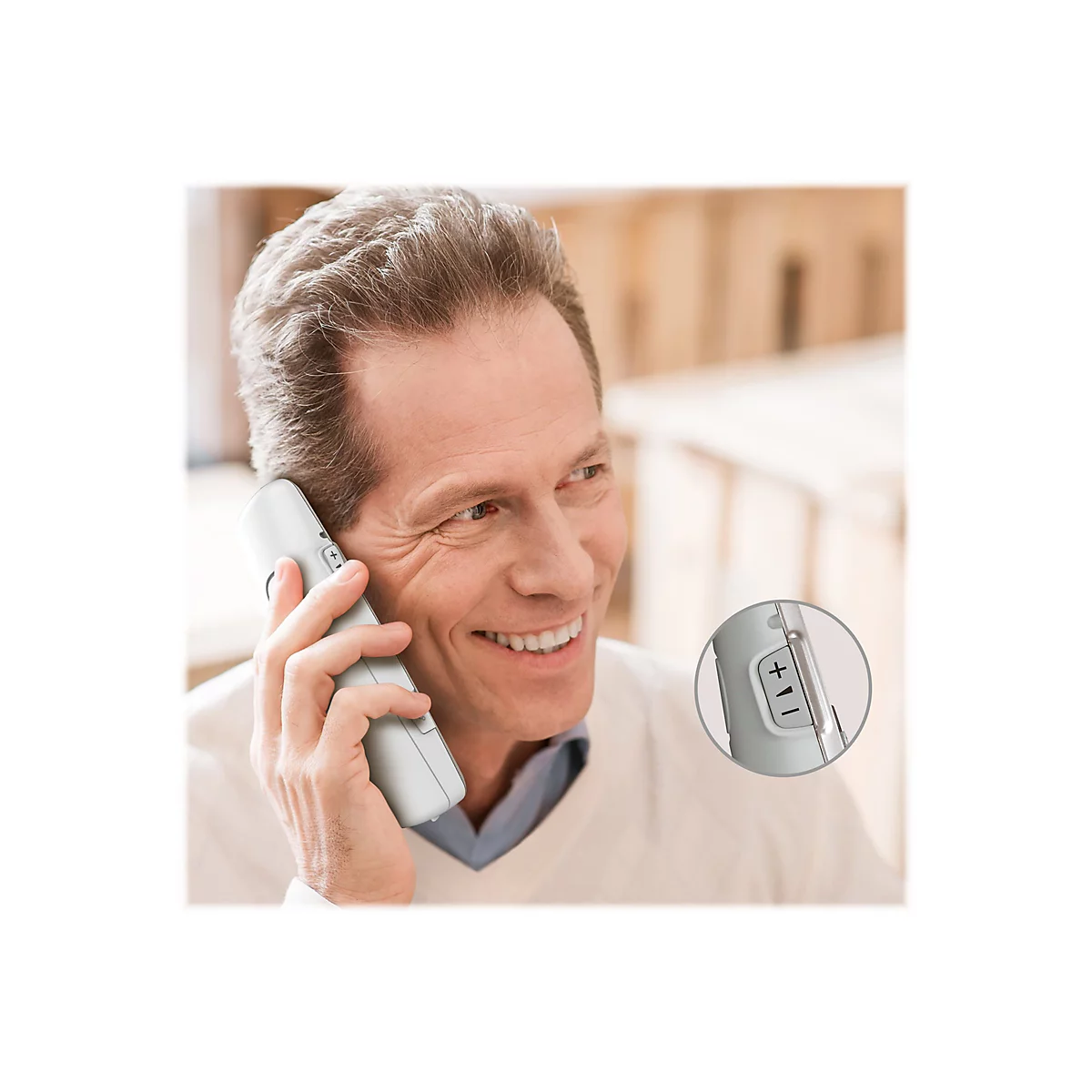 Ein lächelnder Mann telefoniert, hält ein weißes Telefon ans Ohr. Nahaufnahme zeigt das Telefon mit Lautstärketasten.