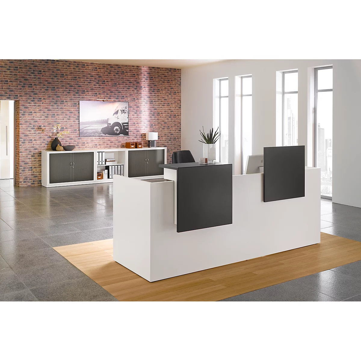 Réception moderne dans une ambiance lumineuse, devant un mur de briques. Plancher en bois, comptoir avec éléments noirs. Meuble de rangement en arrière-plan.