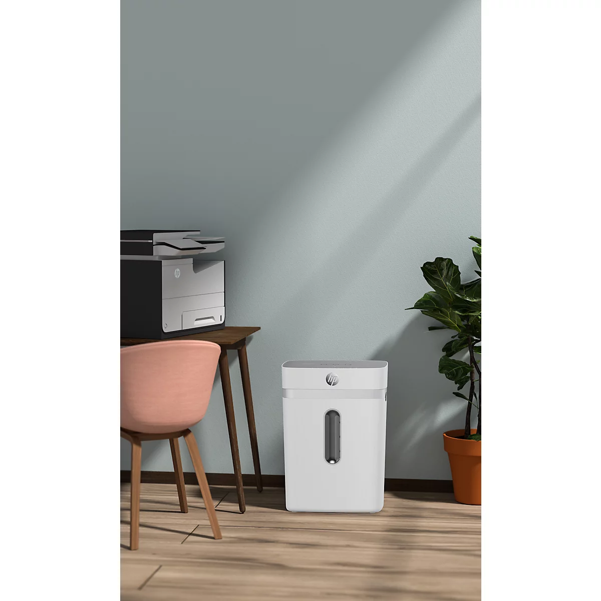 White paper shredder in an office with chair, printer, and plant. The room is blue and has a wooden floor.