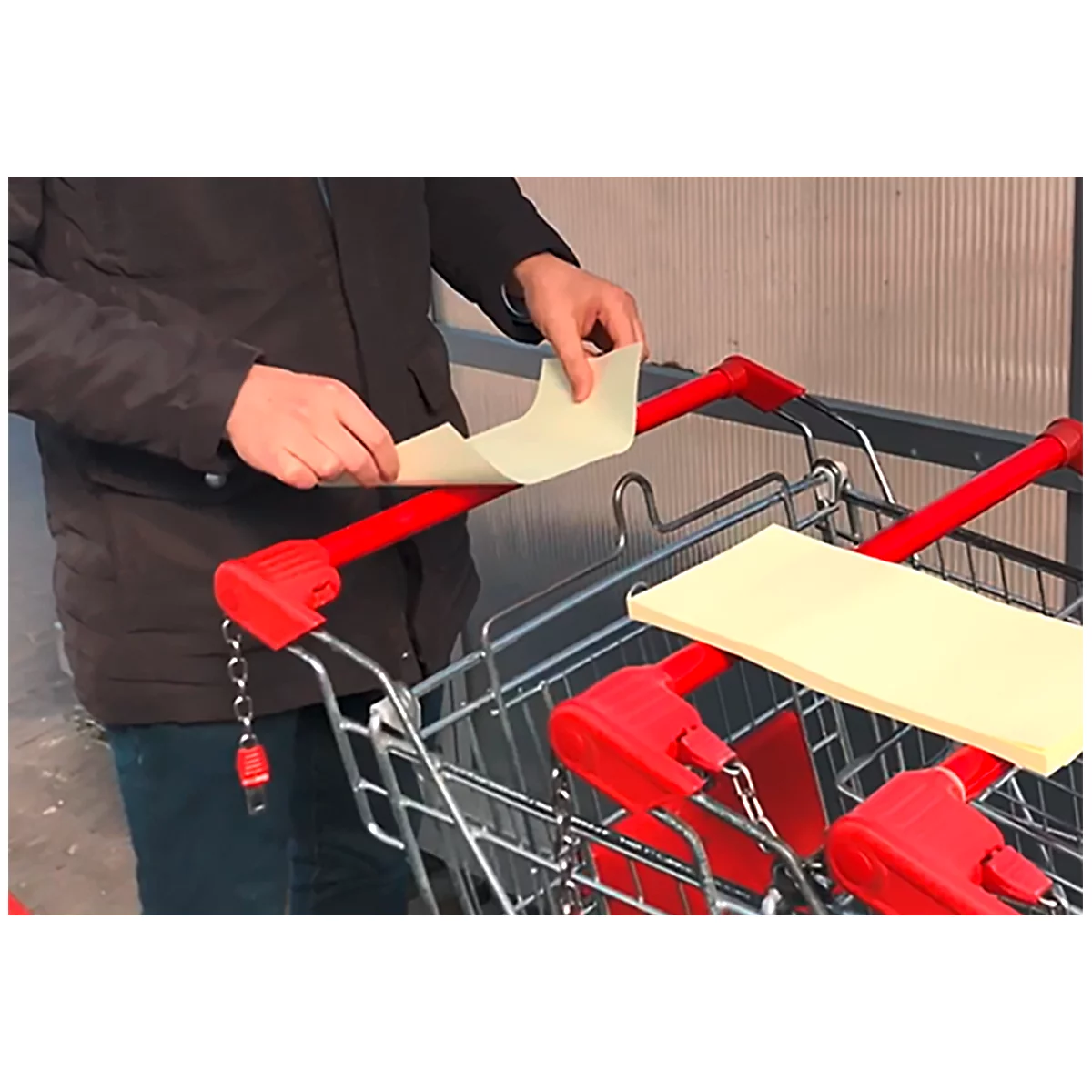 Une personne place du papier sur la poignée d'un chariot de magasinage. Poignée et support rouges.
