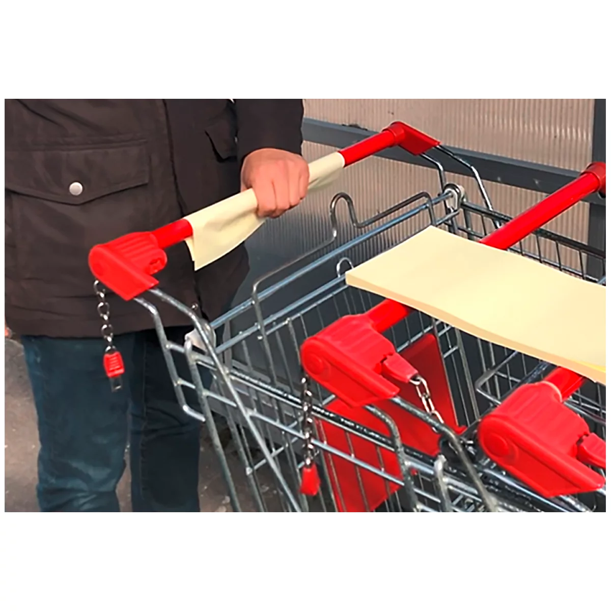 Personne tenant un chariot de magasin par la poignée. La poignée est rouge avec une fixation beige.