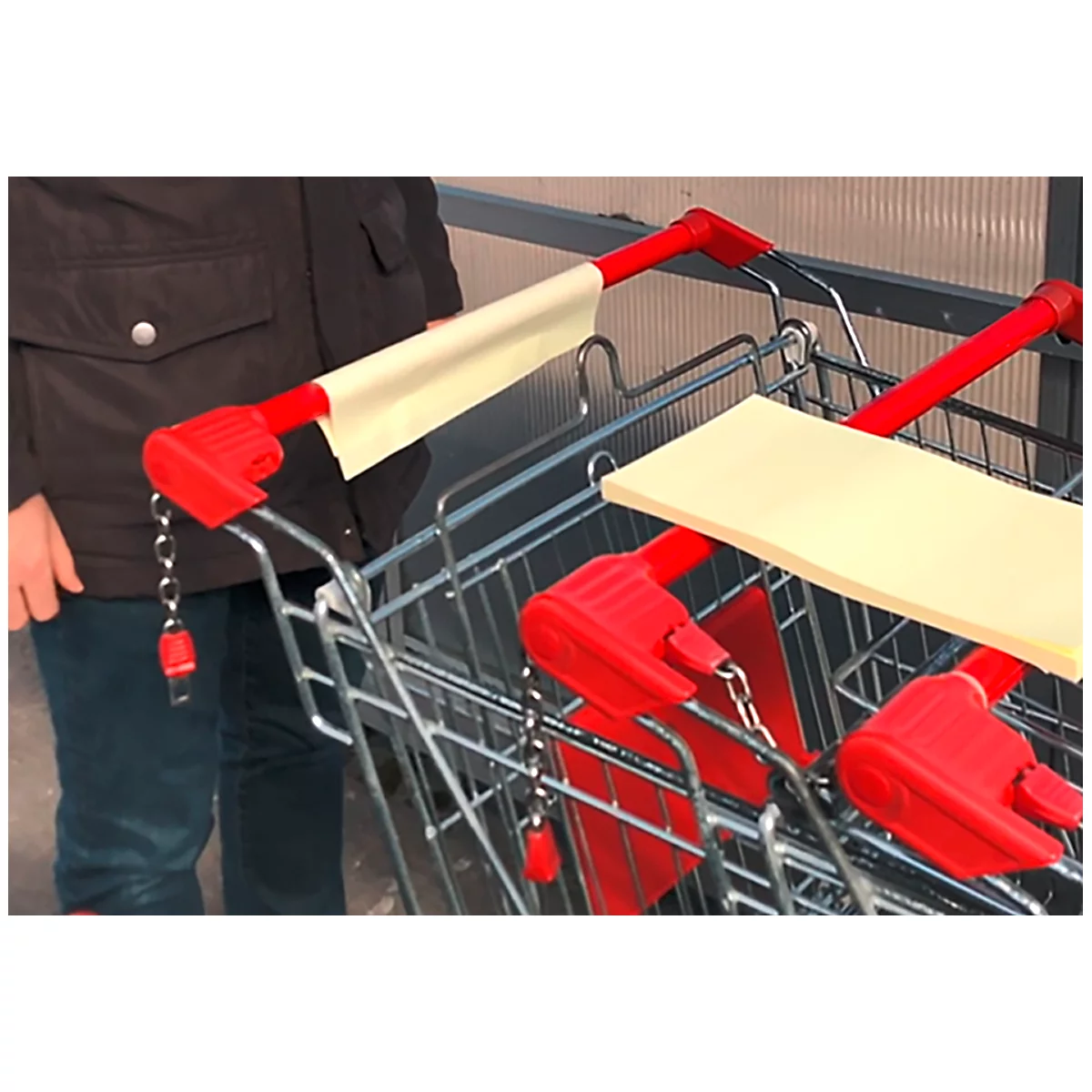 Gros plan sur les poignées de chariots de supermarché, avec des coussinets en papier jaune pour la désinfection. Une personne tient le chariot.