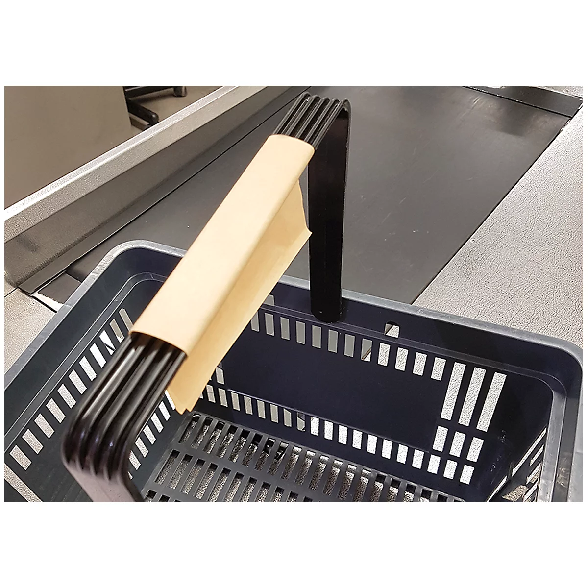 Un panier d'achat noir avec une poignée, posé sur un tapis roulant. La poignée est enveloppée de papier.