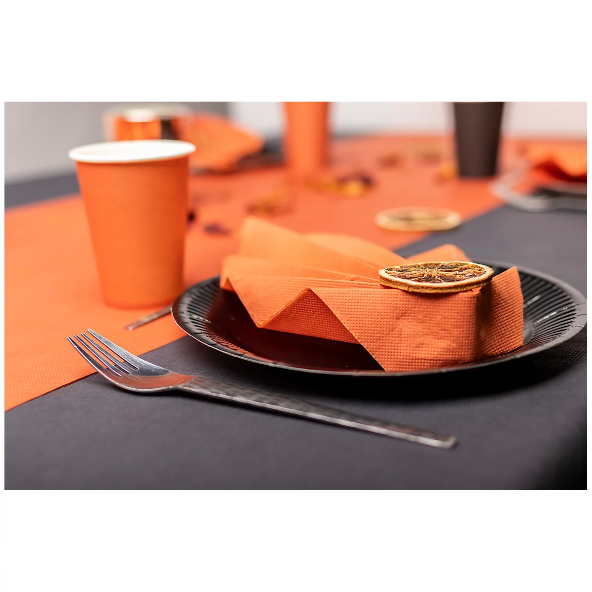Tischdekoration mit orangefarbener Serviette, Teller mit Zitronenscheibe, Gabel und Becher.