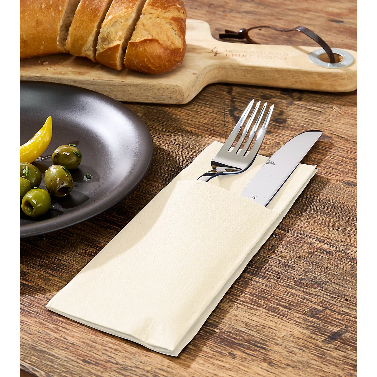 Besteck in Serviette, Oliven, Brot, Zitrone auf Holztisch.