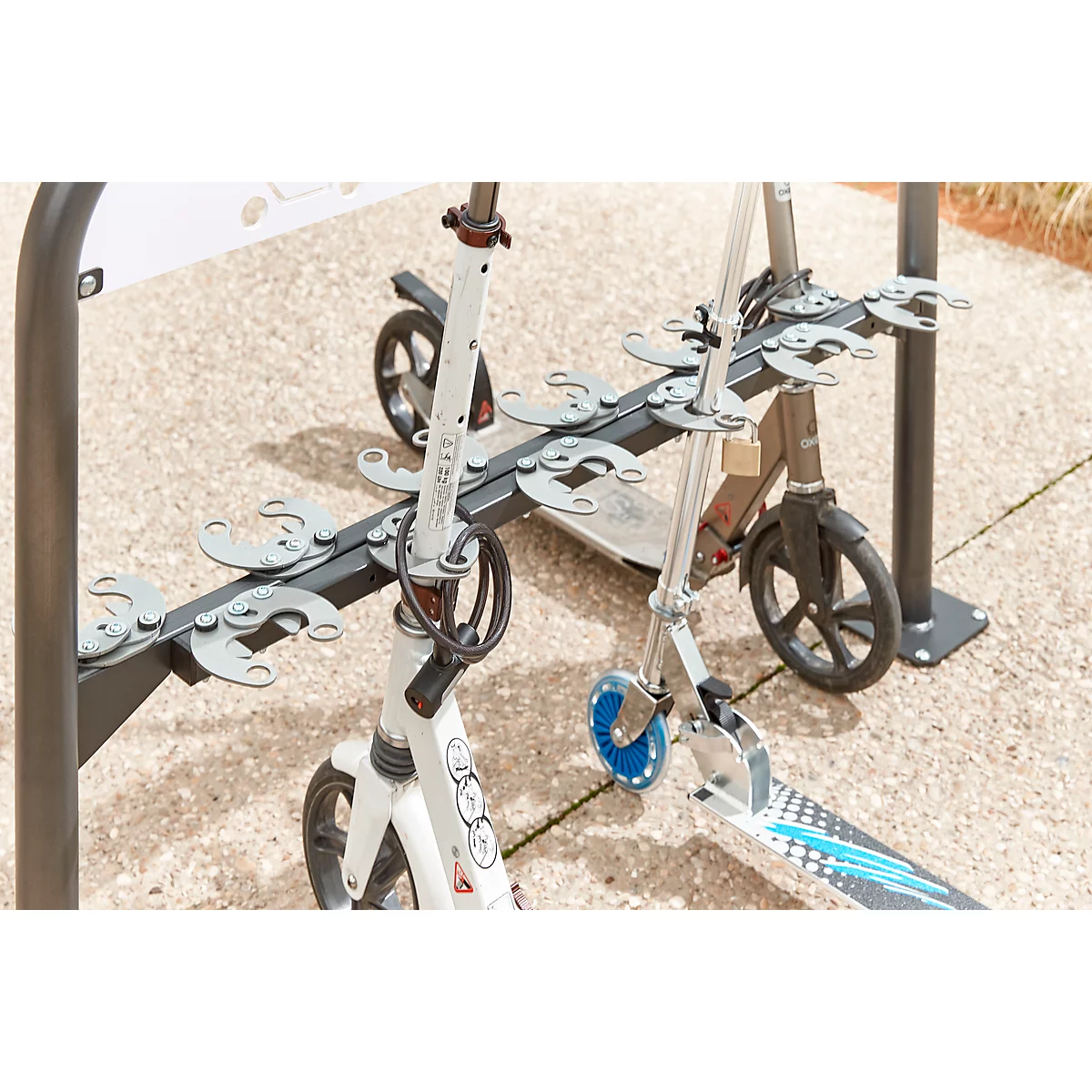 Two scooters in a scooter stand on a paved path. A white scooter stands in front, a gray one behind.