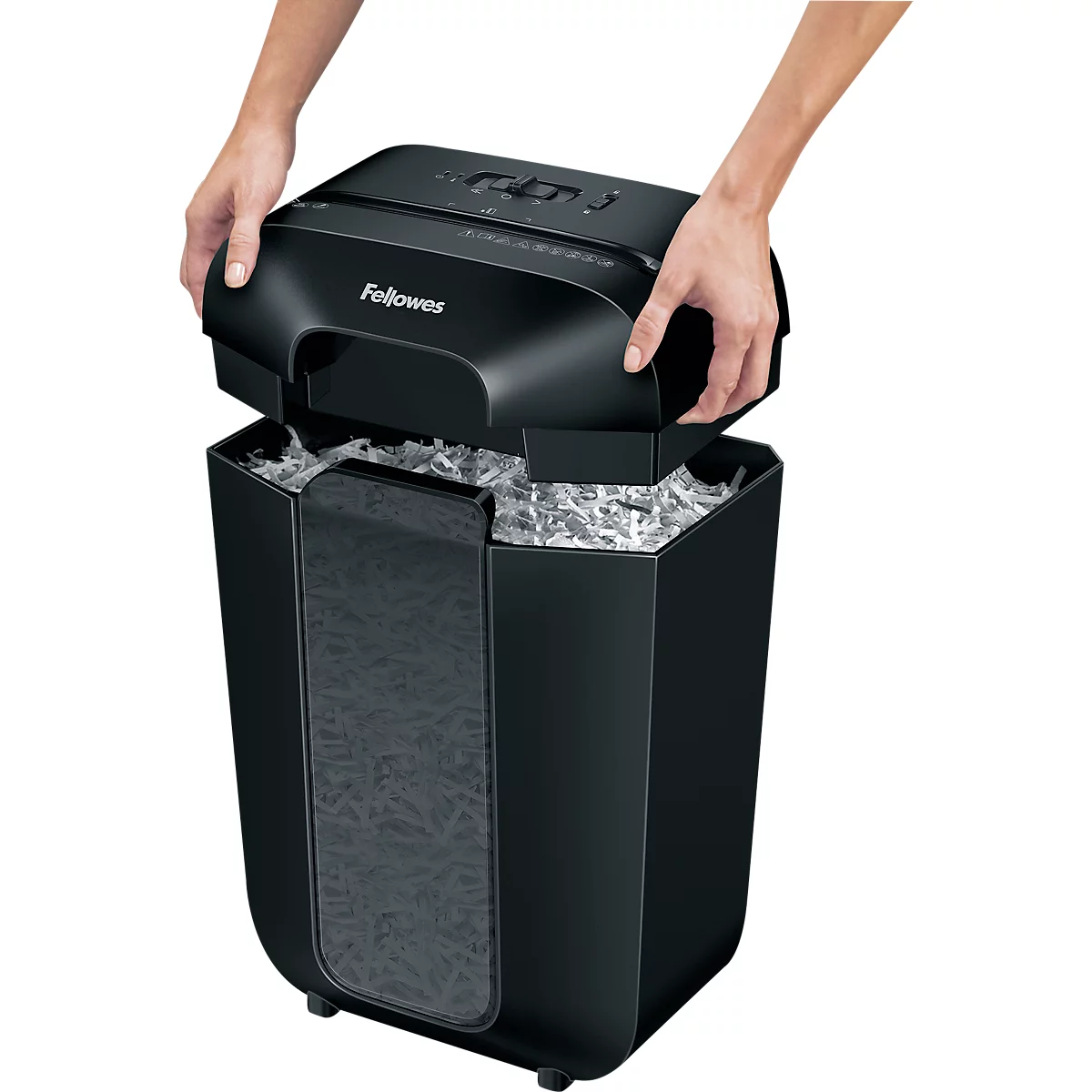 Hands lifting the black paper shredder top. Filled paper shreds underneath. The word Fellowes is visible on the device.