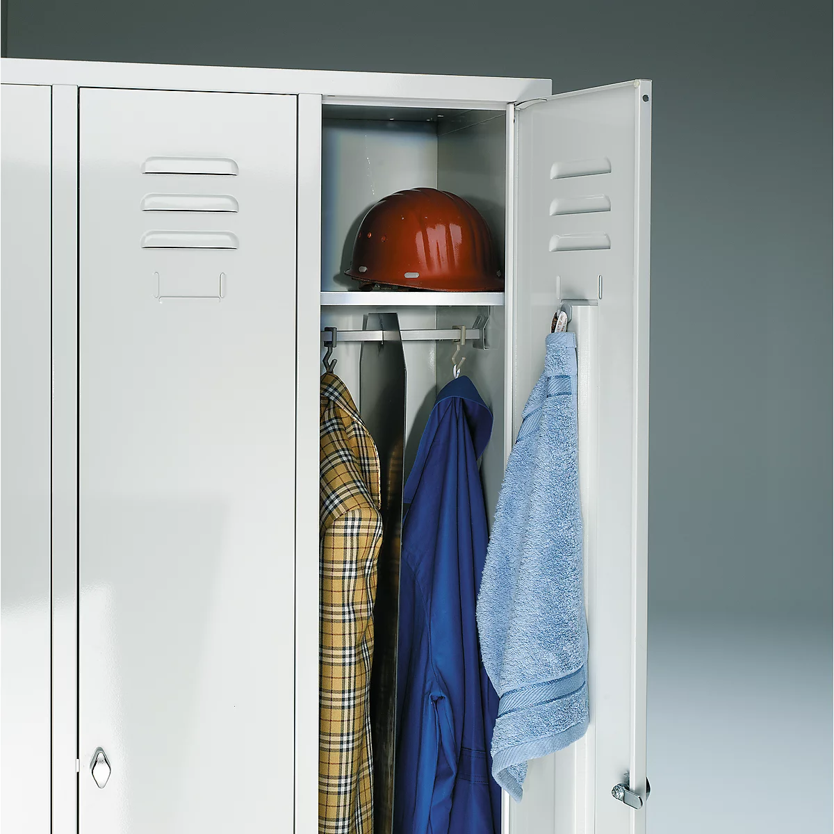 Open white locker with clothes, helmet, and towel. Inside: shirt, jacket, blue towel, and brown helmet.
