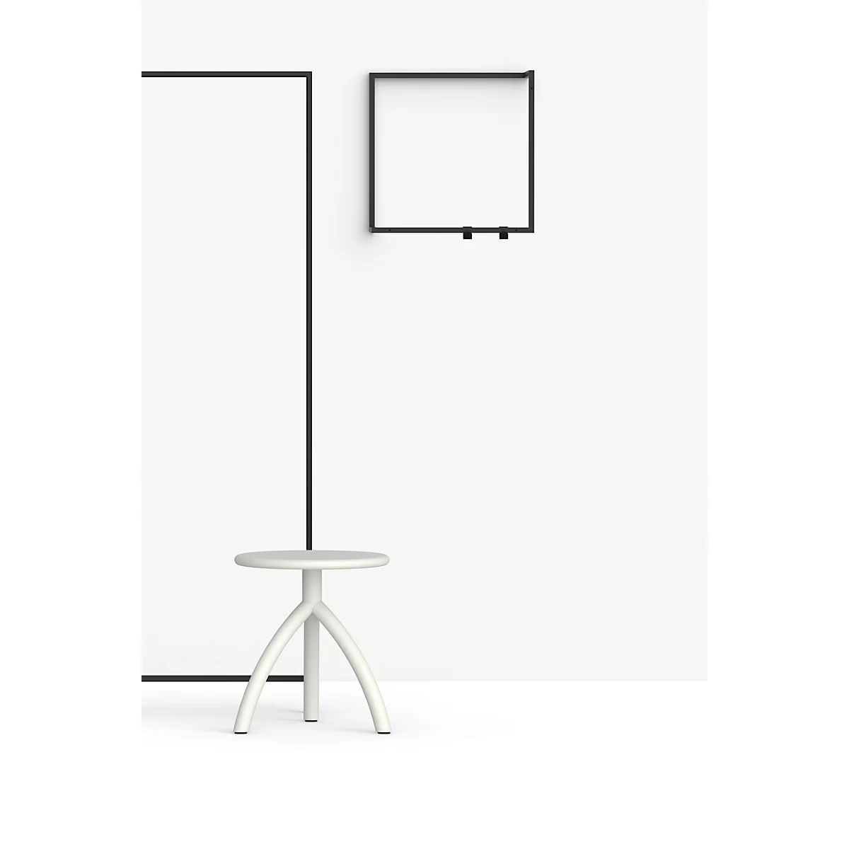 Tabouret gris clair à trois pieds devant un mur blanc avec cadre et étagère noirs.