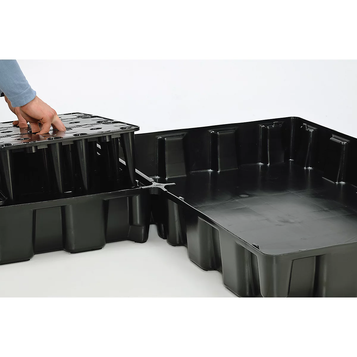 Eine Person platziert eine schwarze Kunststoffplatte auf einer anderen schwarzen Kunststoffplatte. Die Platten sind rechteckig und haben eine wabenartige Struktur.