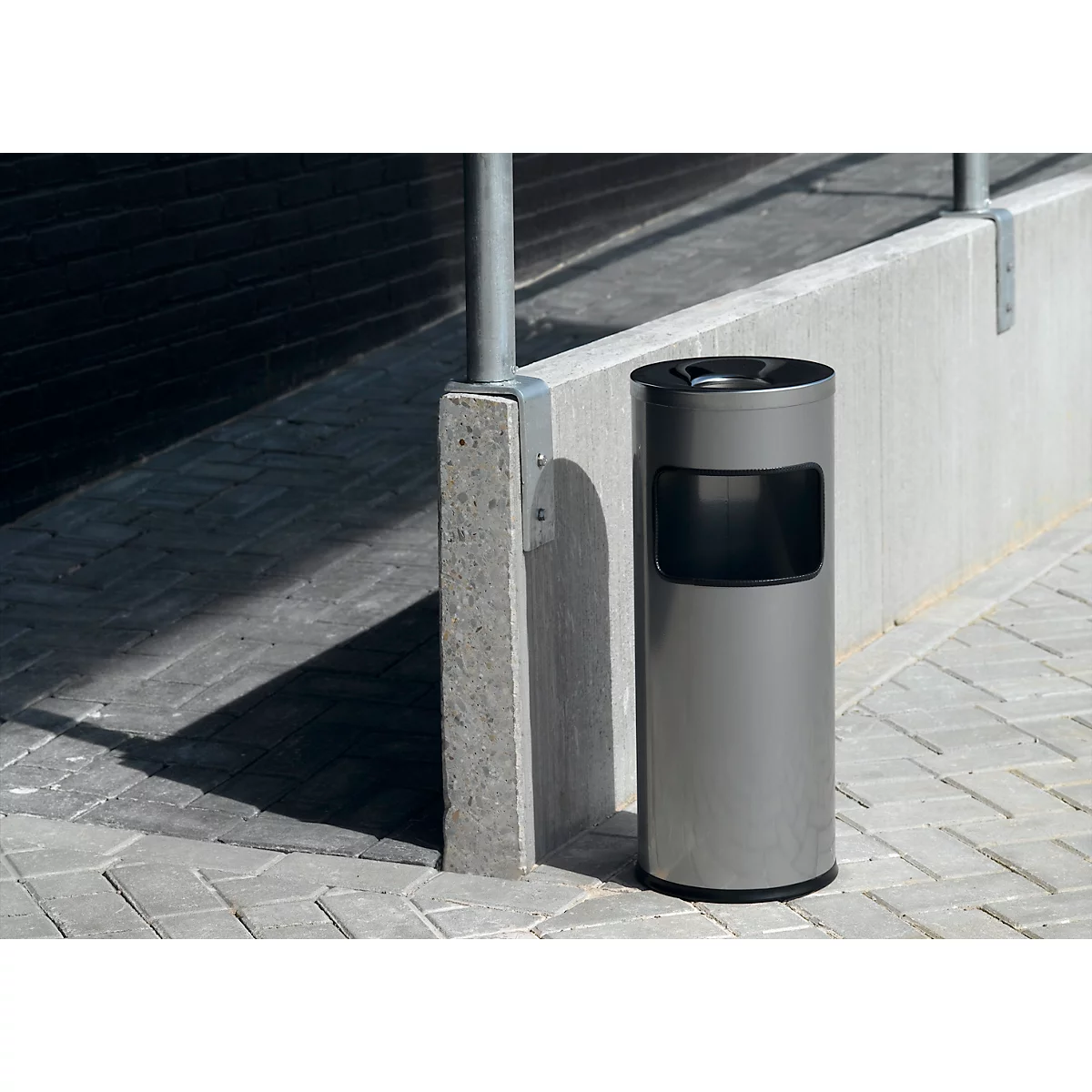 Gray trash can on a paved walkway next to a concrete pillar.