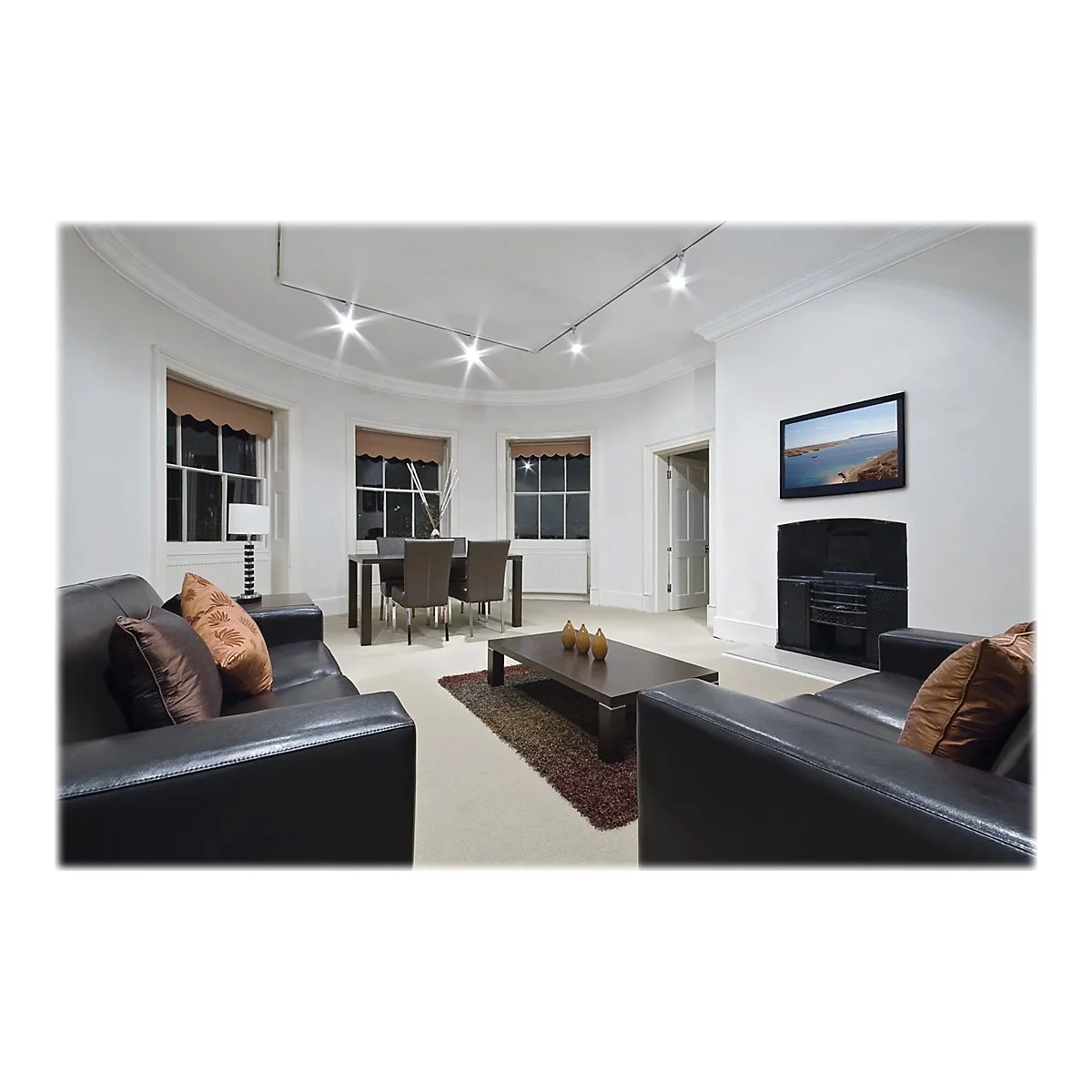 Wohnzimmer mit schwarzem Ledersofa, Fernseher, Kamin und Fenster. Ein Tisch mit Stühlen und Kaffeetisch ist auch zu sehen.