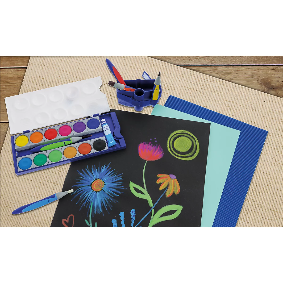 Ein Malkasten mit Pinseln und bunten, auf schwarzem Papier gemalten Blumen auf einem Tisch.