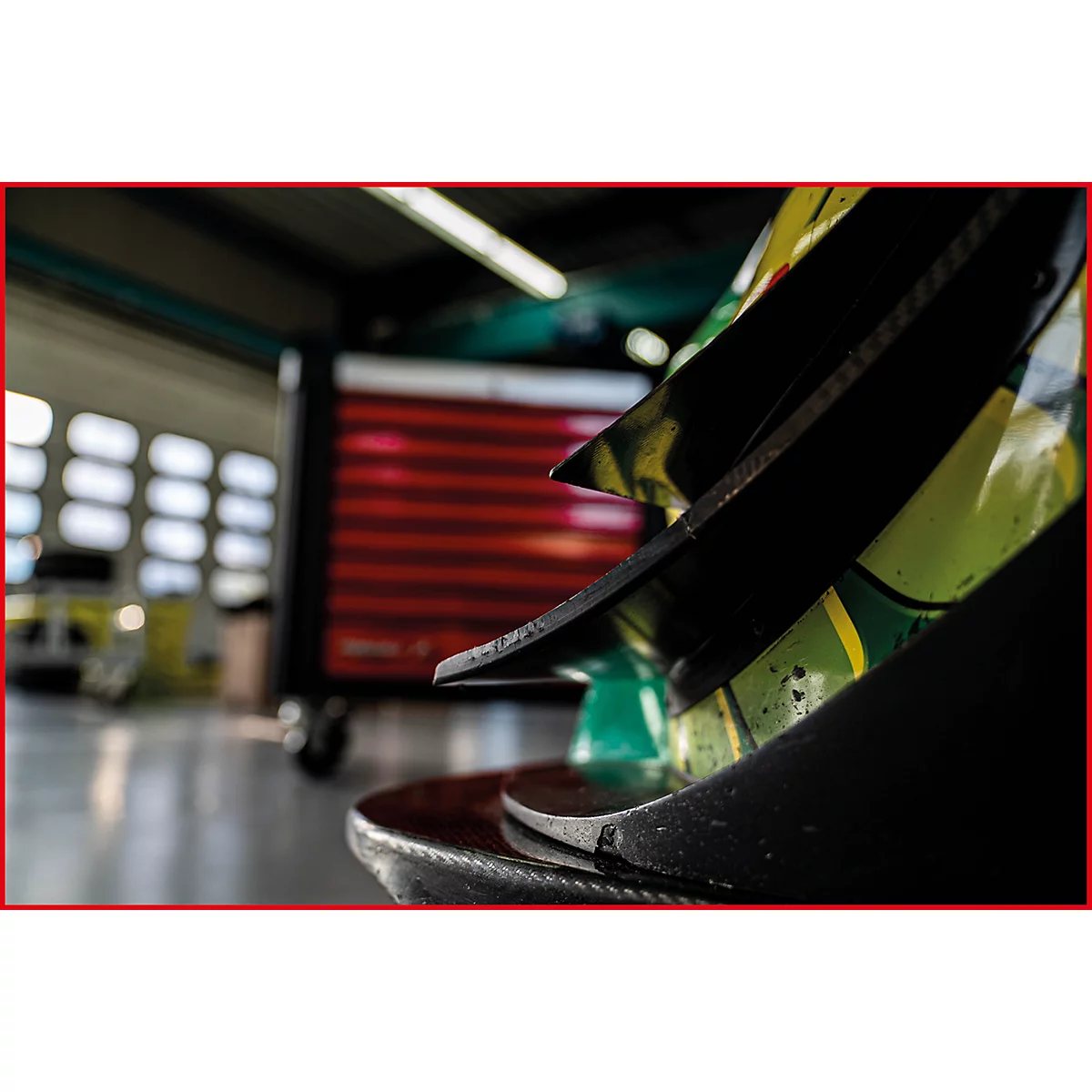 Detailaufnahme eines schwarzen Teils eines Rennwagens. Im Hintergrund verschwommene Garage.