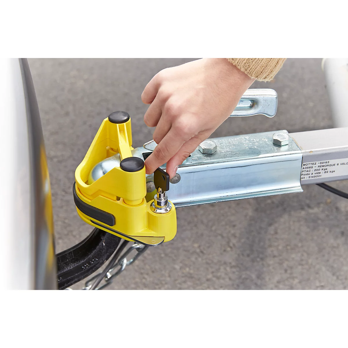 Person locking a yellow lock on a trailer coupling with a key.