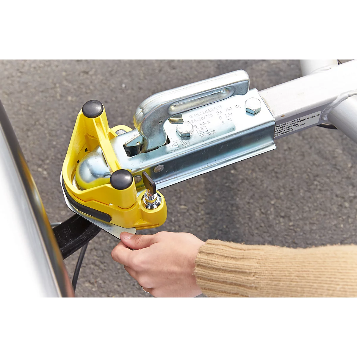A person is operating a yellow trailer hitch lock on a silver trailer hitch.