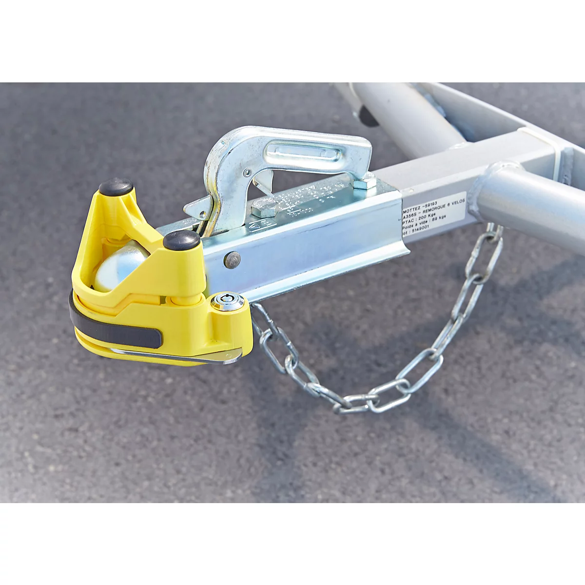 Close-up of a trailer hitch. Yellow housing, silver metal, safety chain.
