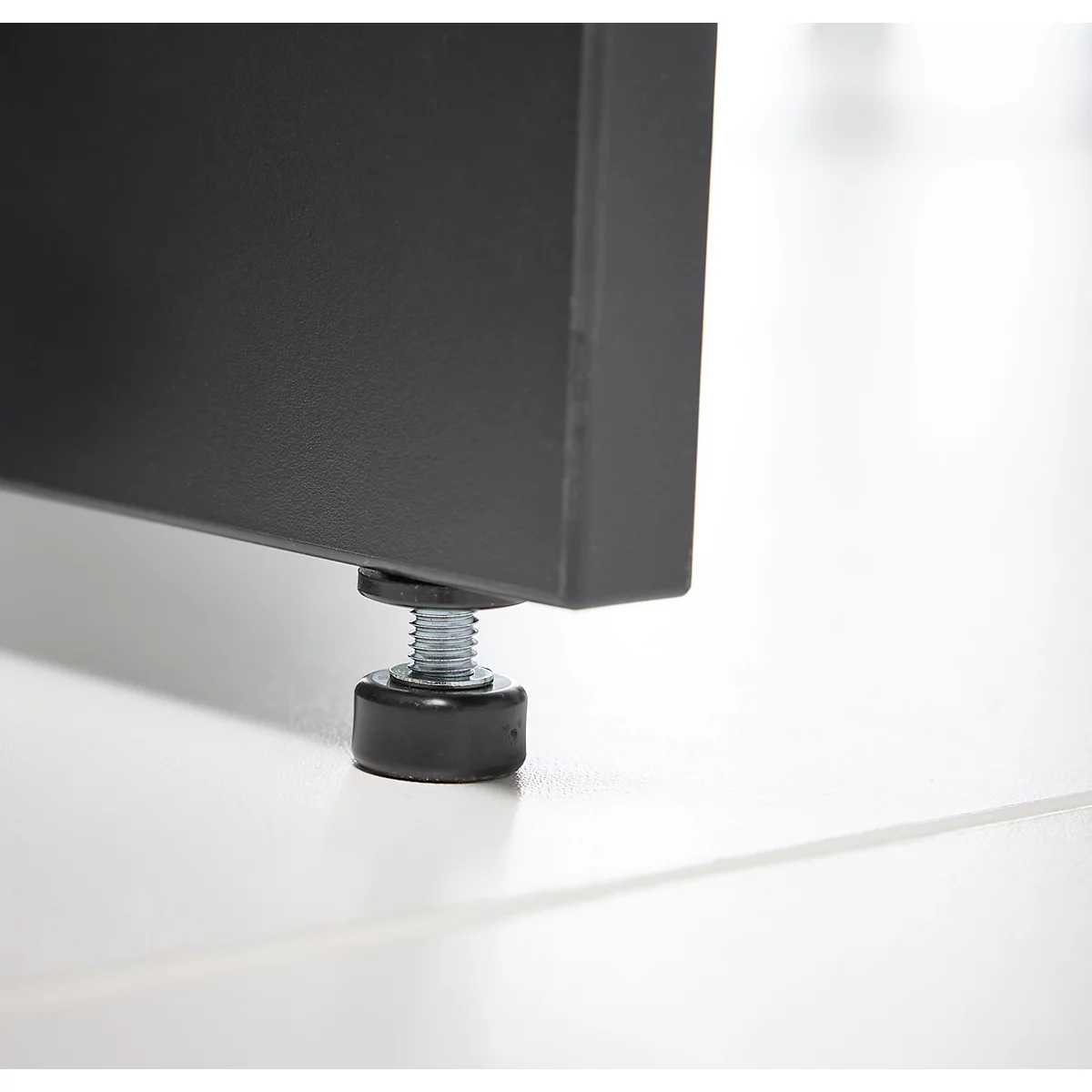 Gros plan : pied en métal noir avec pied de réglage. La base repose sur une surface blanche.