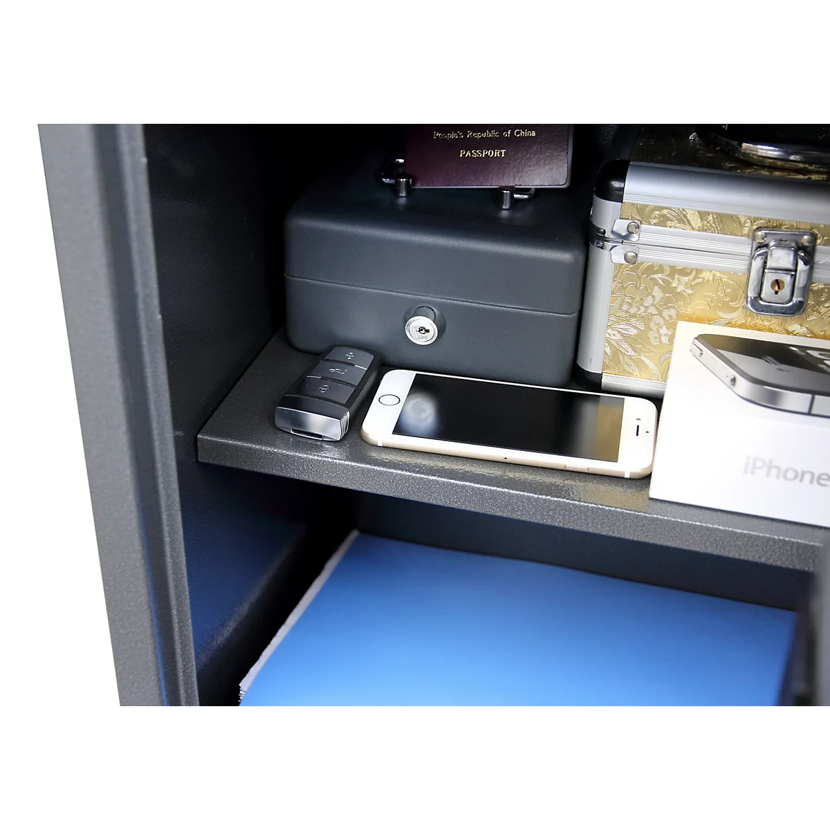 Innenansicht eines geöffneten Tresors mit Kassette, Smartphone, Autoschlüssel und Dokumenten.