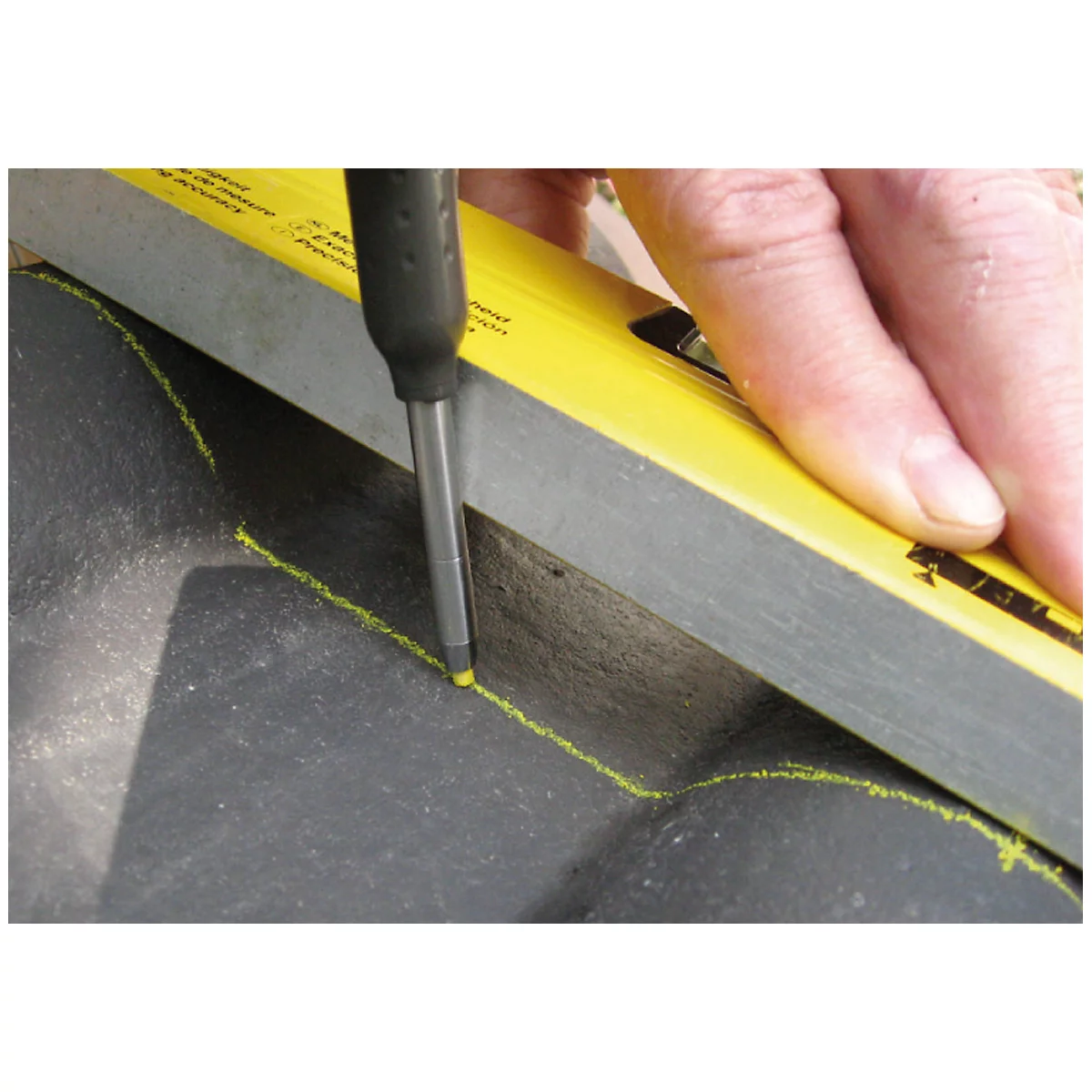 A hand holds a screwdriver and a spirit level to make a mark on a dark surface.