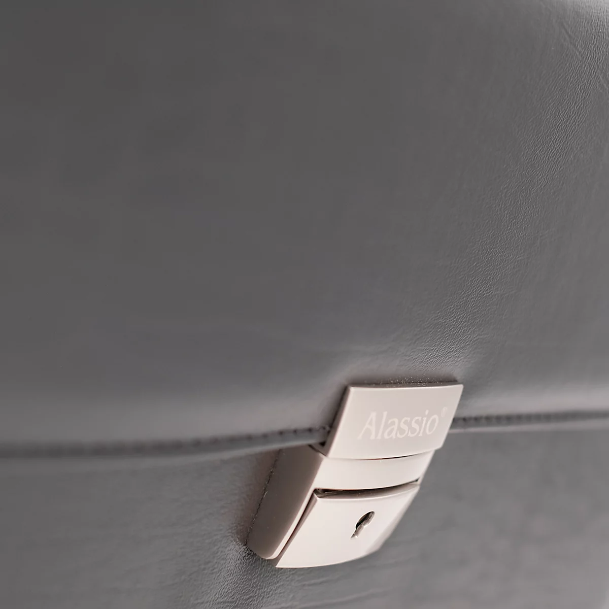 Detailaufnahme einer grauen Ledertasche mit silbernem Schloss, auf dem "Alassio" steht.