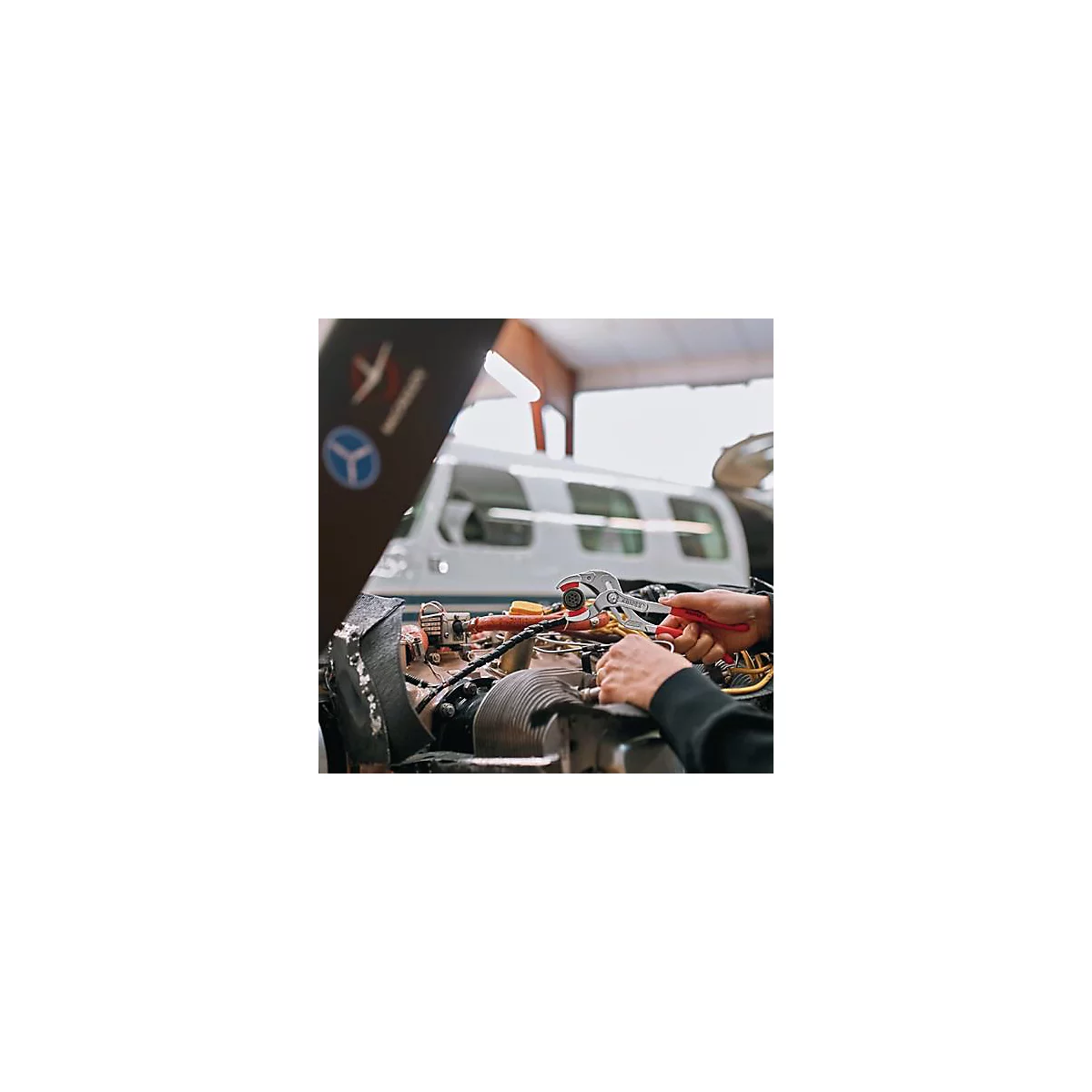 Un mécanicien répare un moteur d'avion avec une pince. En arrière-plan, un avion dans un atelier.